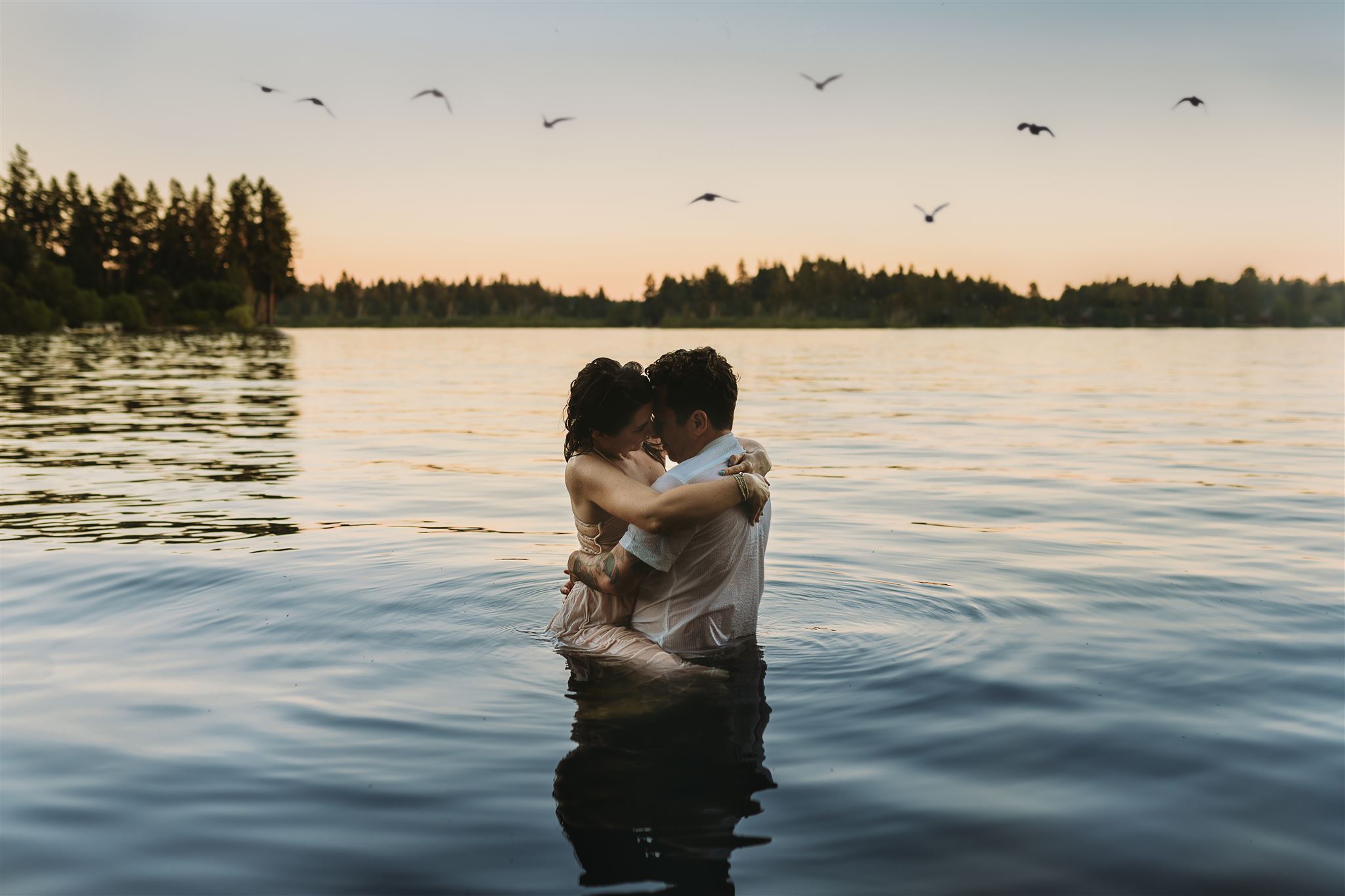 engaged couple holding eachother in a lake while birds fly overhead