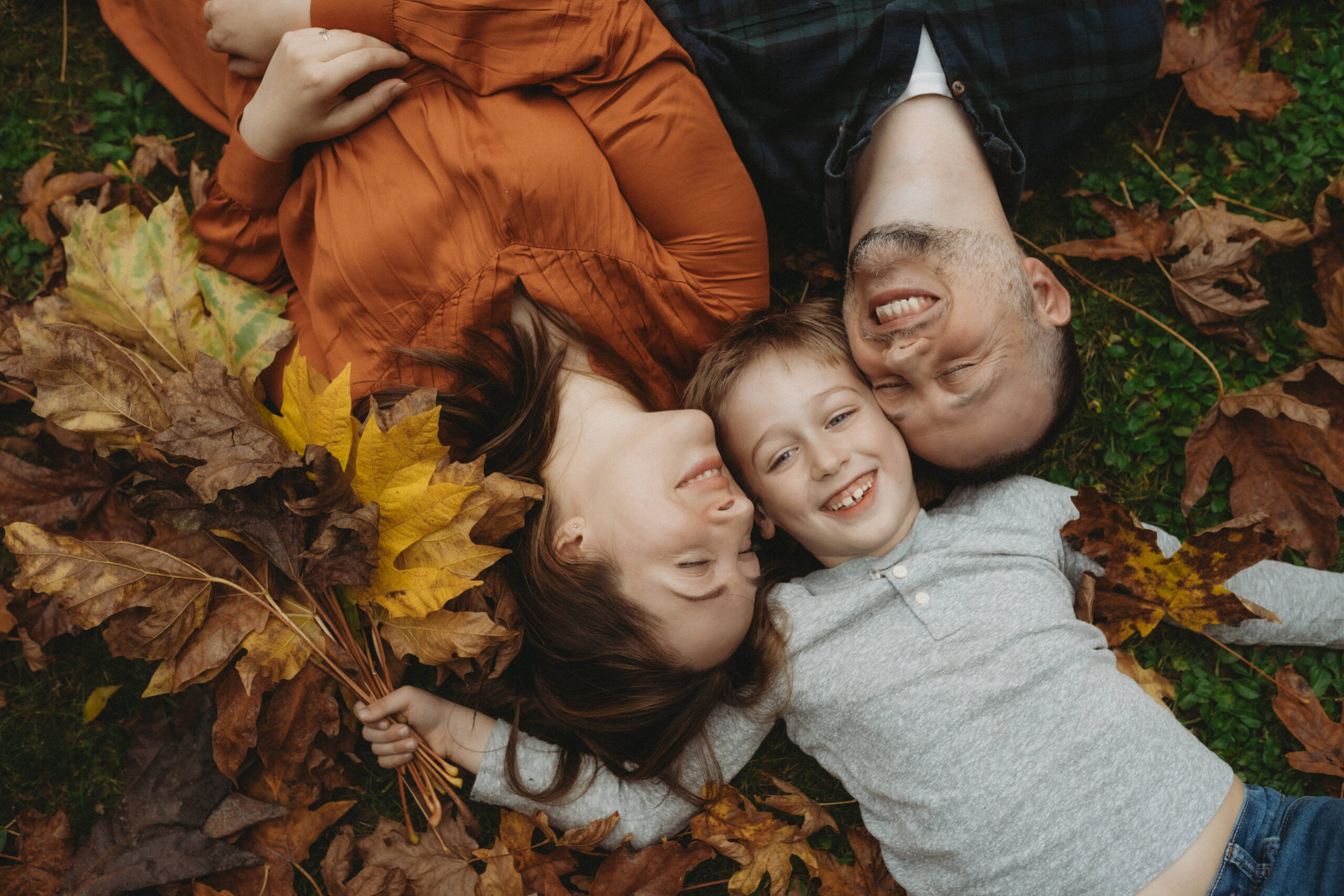 Family lying on ground in leaves.